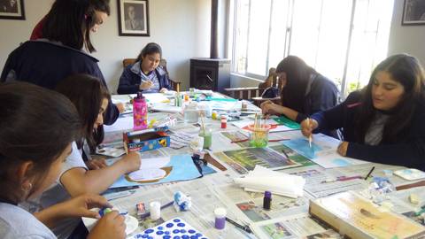 Un grupo de jóvenes está pintando y creando arte en una mesa llena de materiales y papeles.