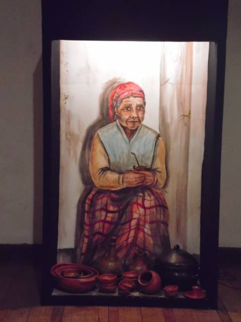 Una anciana sentada, con una expresión serena, rodeada de piezas de cerámica.