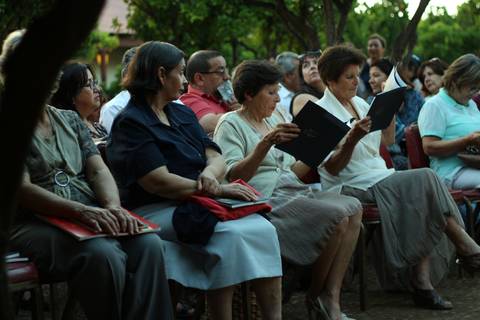 Un grupo de personas sentadas al aire libre, leyendo en sus carpetas durante un evento social.