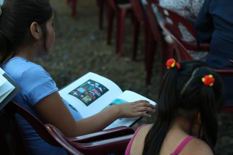 Una niña sentada con un libro en las manos mientras observa a su alrededor.