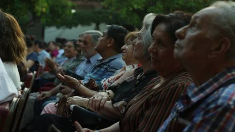 Un grupo de personas mayores observa un evento al aire libre con interés.
