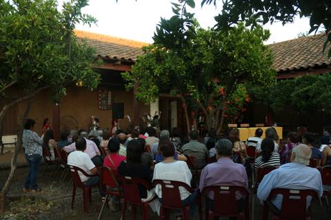 Una multitud observa una presentación cultural en un espacio al aire libre rodeado de árboles y un ambiente acogedor.