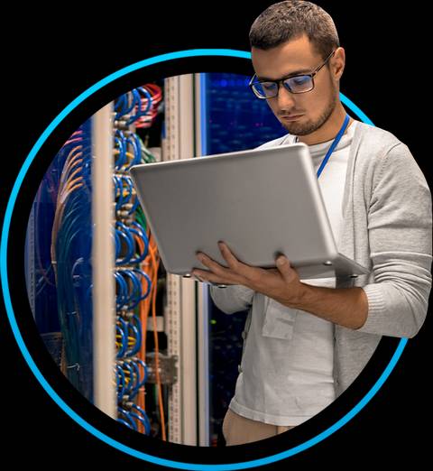 Un hombre trabaja con un portátil en un entorno de servidor, rodeado de cables de red.