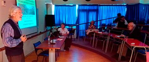 Una conferencia sobre temas variados con un orador y una pequeña audiencia en un salón iluminado.