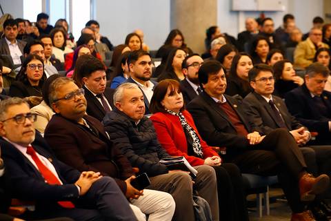 Una multitud de personas sentadas en un evento formal escuchando atentamente.