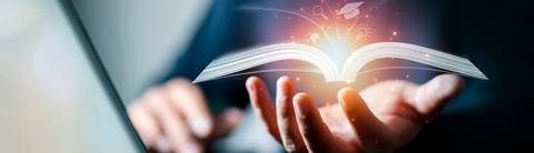 Una mano sostiene un libro abierto con destellos de luz que emanan de sus páginas.