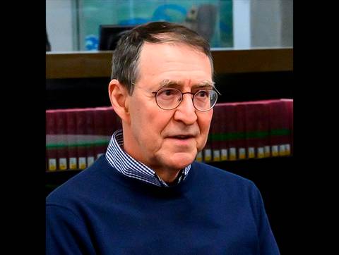 Un hombre con gafas está sentado y parece estar en una conversación seria.