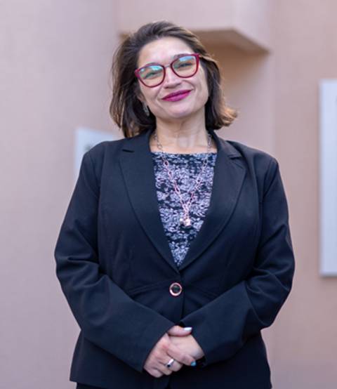 Una mujer sonriente en un entorno profesional, vestida con traje y gafas.