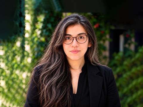 Una mujer con lentes y cabello largo posa frente a un fondo verde.