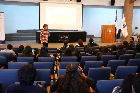 Un joven presenta frente a un grupo de estudiantes en una sala de conferencias.