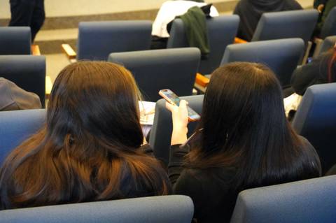Dos chicas mirando sus teléfonos en una sala de clases.