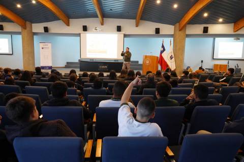 Un docente está presentando frente a un grupo de estudiantes en un auditorio.