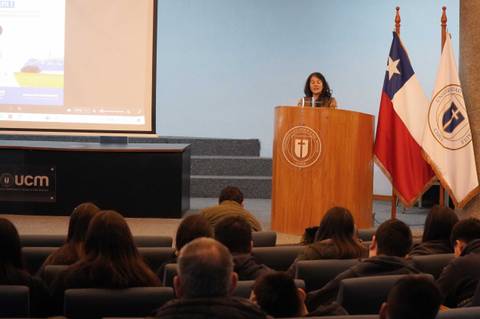 Una persona dando una charla en un auditorio con banderas chilenas de fondo.