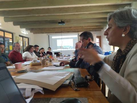 Un grupo de personas discutiendo en una reunión con proyector y papeles sobre la mesa.