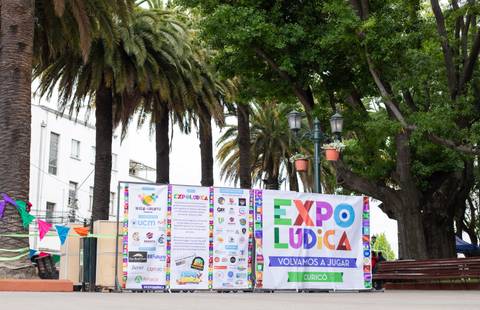Una feria recreativa en un parque con una gran pancarta que invita a jugar.