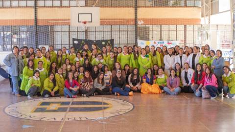 Un grupo grande de mujeres reunidas en un gimnasio, todas con vestimenta colorida y sonrisas en sus rostros.