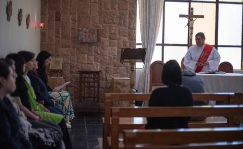 Una misa en una iglesia con un sacerdote y asistentes sentados en bancos.