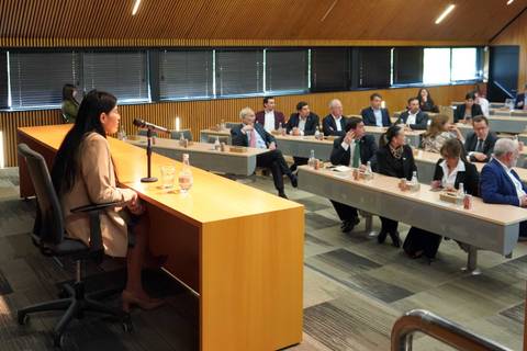 Un grupo de personas escucha atentamente a una mujer mientras ella expone en una sala de conferencias.