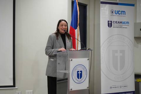 Una mujer sonriente habla desde un podio en un evento en una universidad chilena.