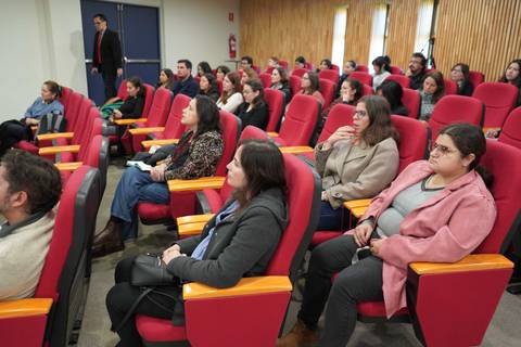 Una audiencia atenta sentada en un auditorio con sillones rojos.