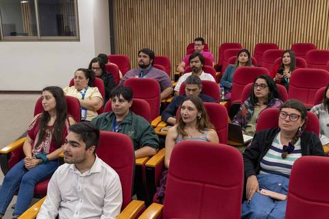 Un grupo de personas sentadas en un auditorio, prestando atención a una presentación.