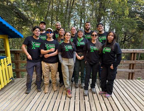 Un grupo de personas jóvenes posando en un espacio al aire libre, todos vistiendo camisetas negras con un diseño verde.