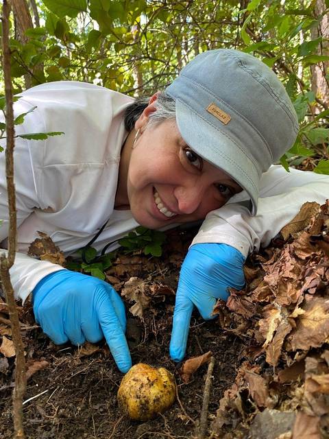 Una mujer feliz señalando un hongo que encontró en el bosque.