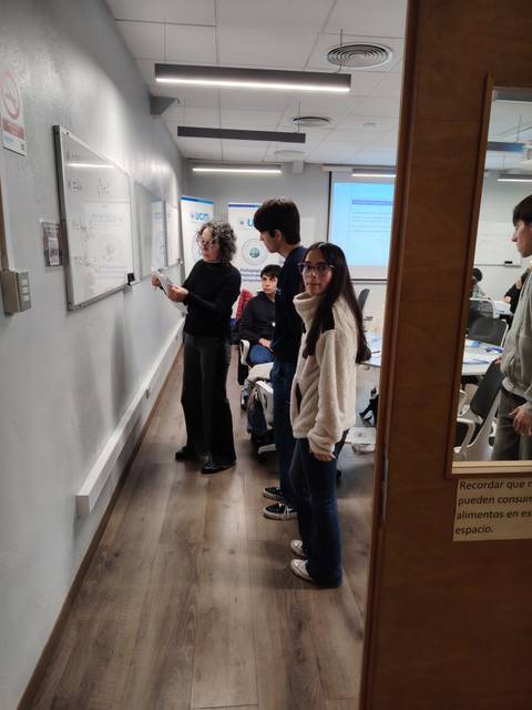 Un grupo de estudiantes en un salón de clases interactuando frente a una pizarra.