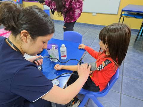Una profesional de la salud está midiendo la presión arterial a un niño en un salón de clases.