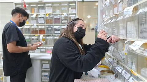 Dos trabajadores en una farmacia organizando medicamentos mientras usan mascarillas.