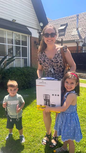 Una mujer y dos niños disfrutan de un día soleado mientras muestran un electrodoméstico en el jardín.