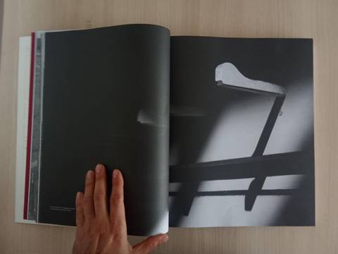 Una mano sostiene una revista abierta con una imagen en blanco y negro de un gancho en una pared.