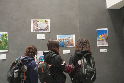Un grupo de jóvenes observa fotografías en una pared mientras están de espaldas.