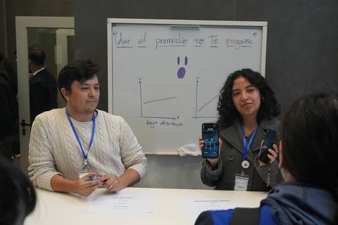 Dos jóvenes presentan un proyecto en una exposición mientras muestran gráficos en sus dispositivos.