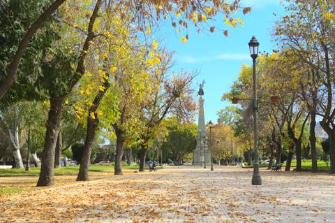 Un hermoso parque con árboles amarillos y un monumento en el centro.