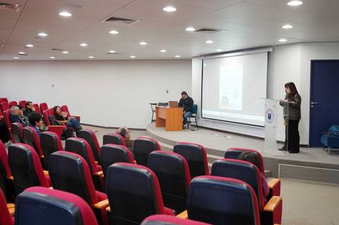 Una sala de conferencia con un presentador frente a un público atento.
