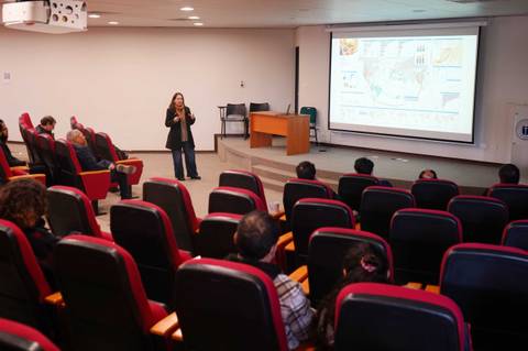 Una mujer presenta en una sala de conferencias con público frente a ella.