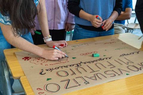 Estudiantes colaborando en la creación de un afiche en un aula.