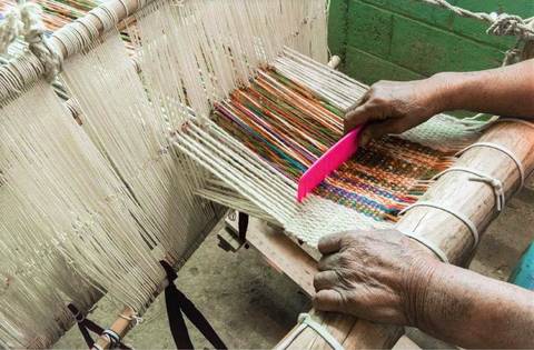 Una persona tejiendo en un telar con hilos de colores brillantes.