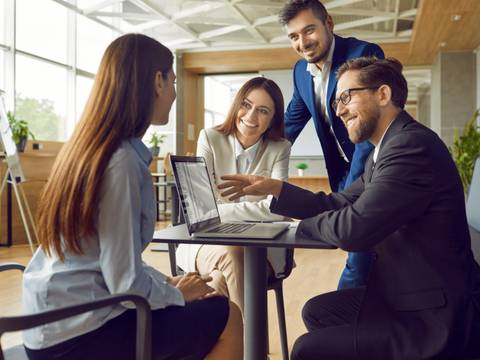 Un grupo de profesionales se reúne en una oficina moderna para discutir ideas frente a un computador.
