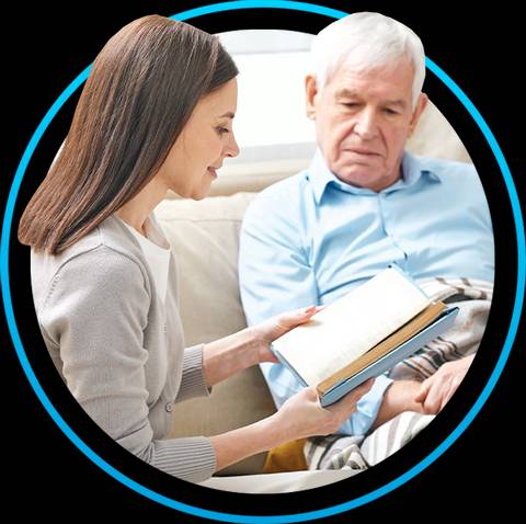 Una mujer lee un libro a un hombre mayor sentado junto a ella.