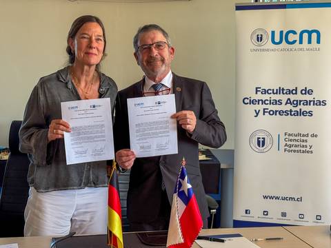 Dos personas sosteniendo documentos en una ceremonia de firma en la Universidad Católica del Maule.