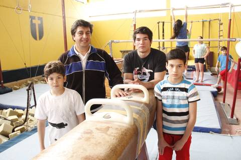 Un grupo de cuatro personas, incluidos dos niños y un adulto, posan frente a un caballo de salto en un gimnasio de gimnasia.