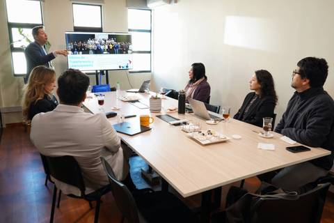Un grupo de personas se encuentra en una reunión en una sala de conferencias mirando una presentación proyectada.