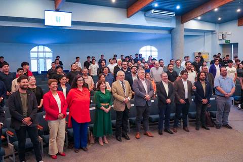 Un grupo grande de personas en un evento formal en un salón con asientos.