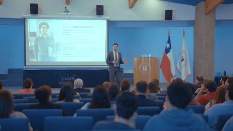 Un expositor presenta un tema frente a una audiencia en un auditorio chileno.