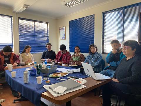 Un grupo de personas participando en una reunión en una sala con ventanas y mesas.