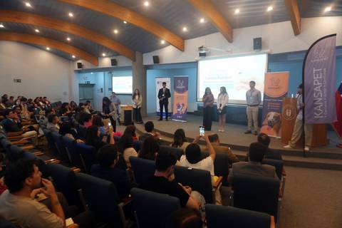 Un grupo de personas presenta en un evento frente a una gran audiencia en una sala con luz natural.