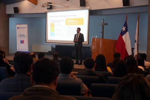Un expositor presentando en un auditorio con la bandera de Chile de fondo.