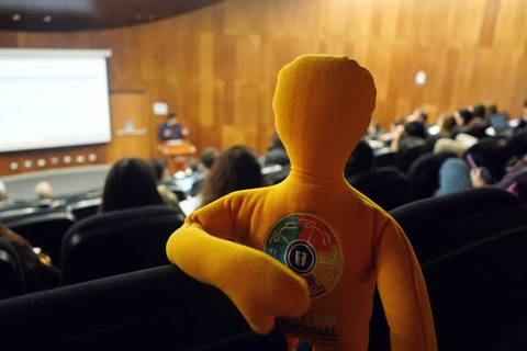 Un monito de peluche observa a la audiencia en una charla en un auditorio.
